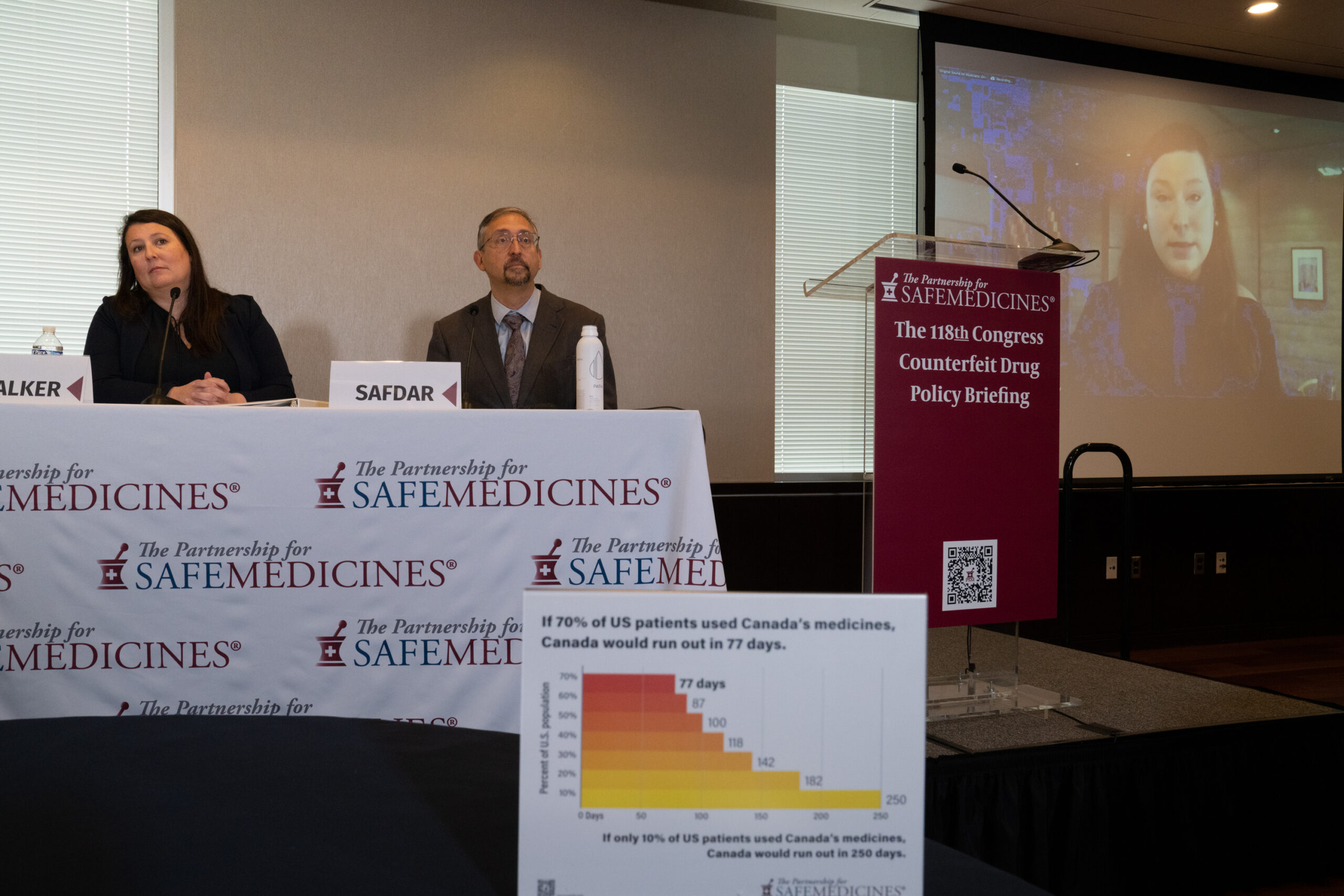 Two panelists at a table covered with white tablecloth bearing PSM's logo. A screen to the right displays the third panelist in conversation