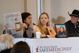 Two women and a man in a black cowboy hat are seated at a table with a white tablecloth emblazoned with PSM's logo. One of the woman is holding up a news paper.