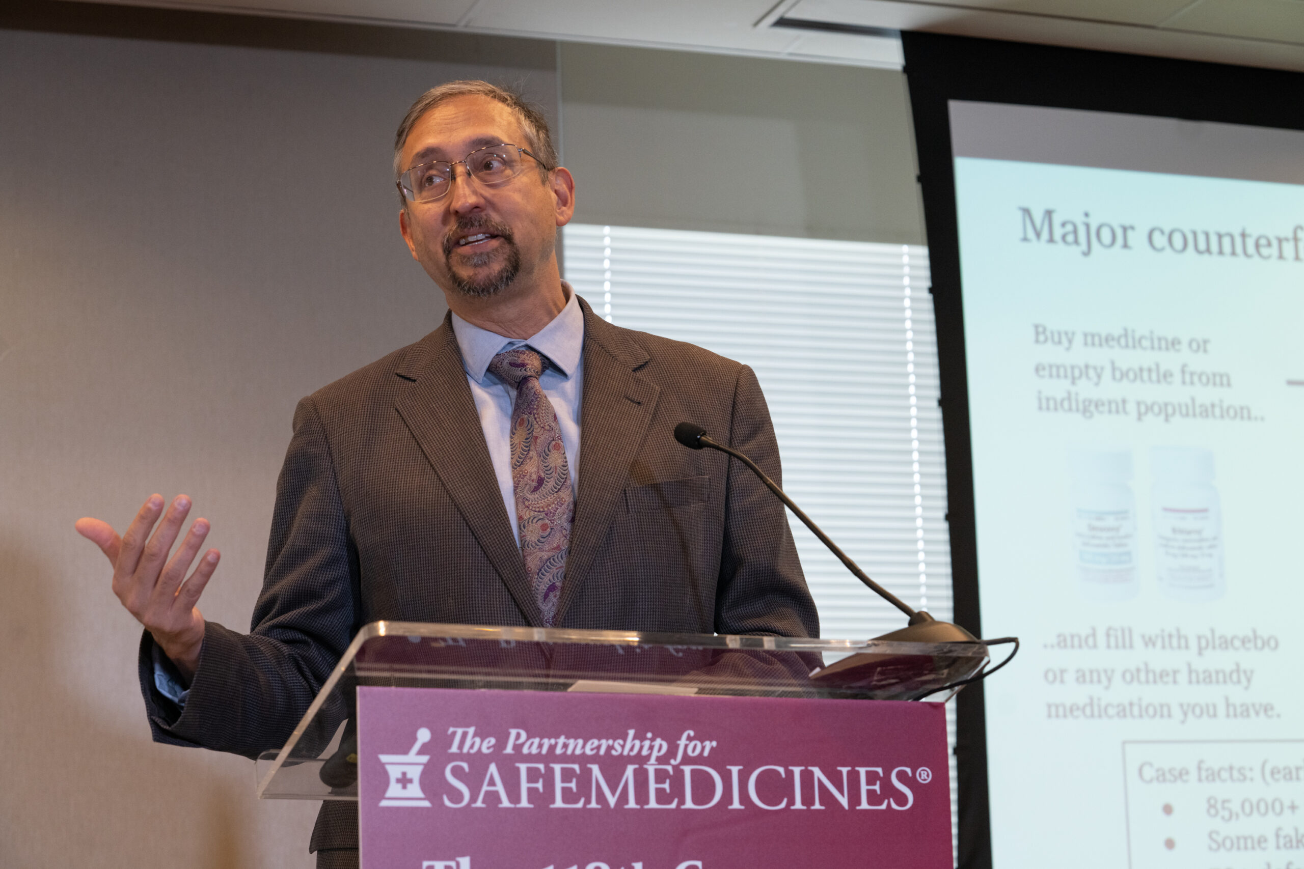 Man gesticulating at a podium with the PSM logo visible.