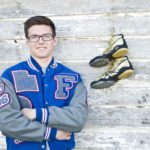 Young man in letter jacket standing in front a wall, wrestling boots, badge and medal alongside him