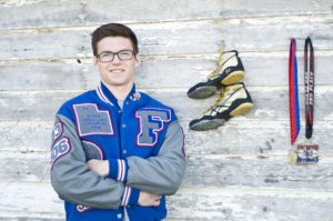 Young man in letter jacket standing in front a wall, wrestling boots, badge and medal alongside him