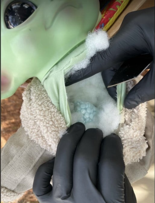 An investigator holds open a baby Yoda toy to how fentanyl pills.