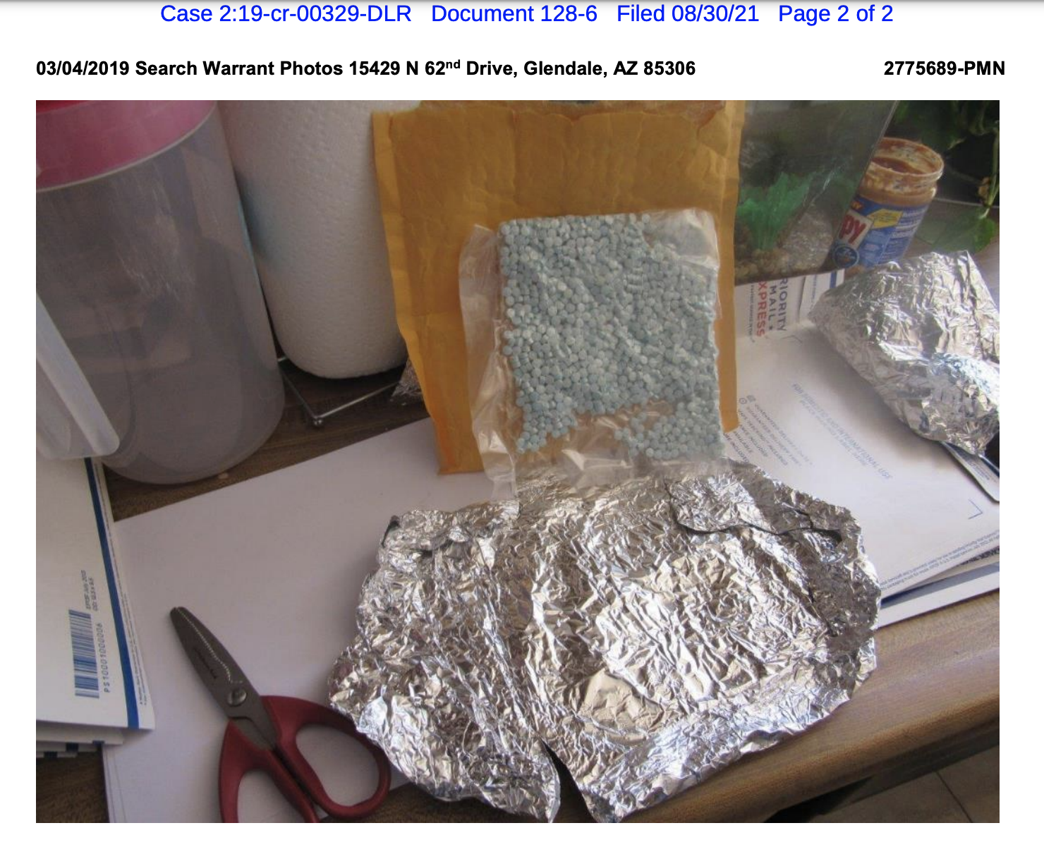 blue pills in sealed plastic propped against a manilla envelope on a surface with tin foil