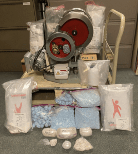 a pill press and clear plastic bags of fentanyl powder and blue pills