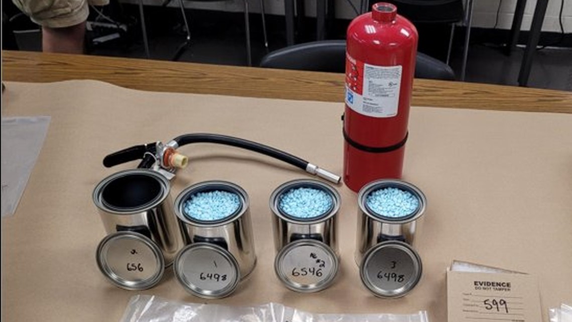 silver cans that contain fentanyl pills next to a red fire extinguisher on a table