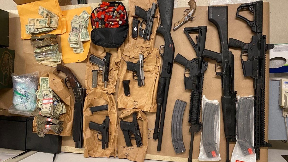Firearms, ammunition, cash and pills laid out on a wooden table