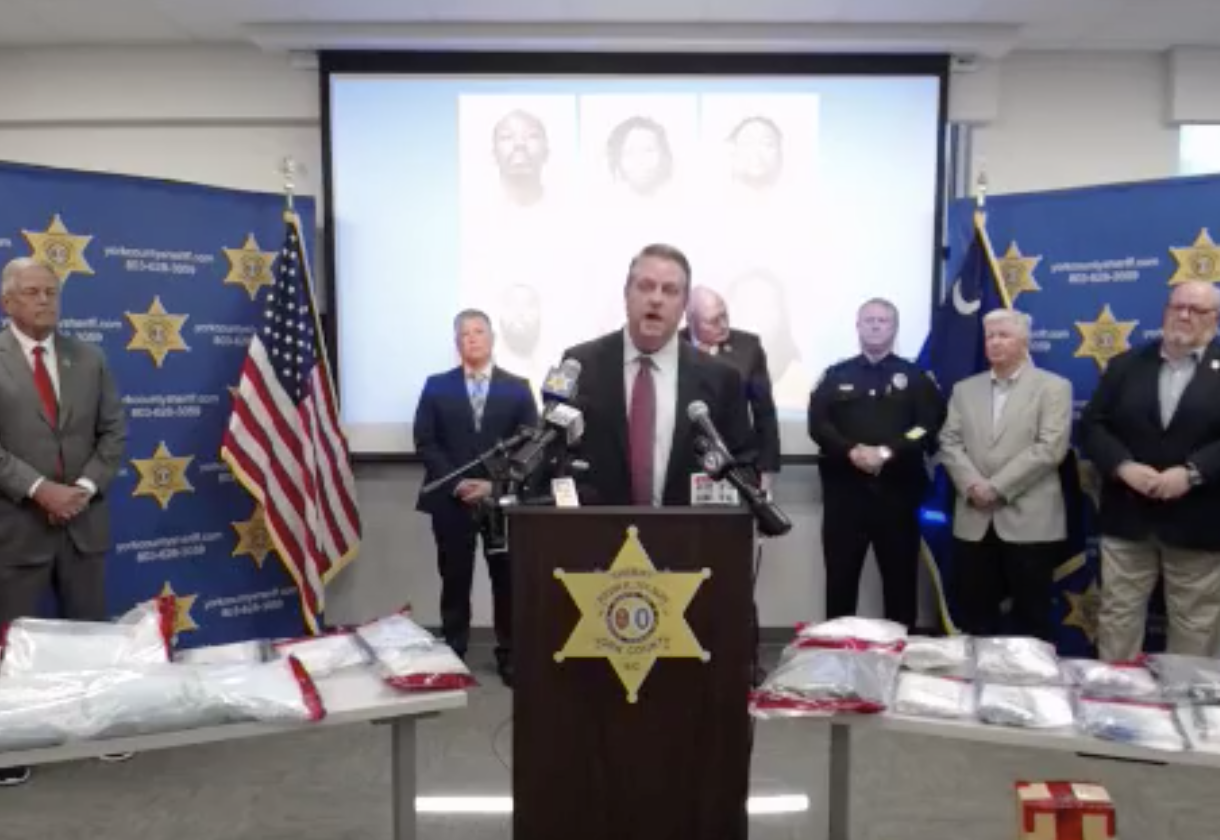 Press conferednce with men standing in front of a projection screen