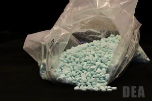 blue pills embossed with M30 spilling out of a plastic bag