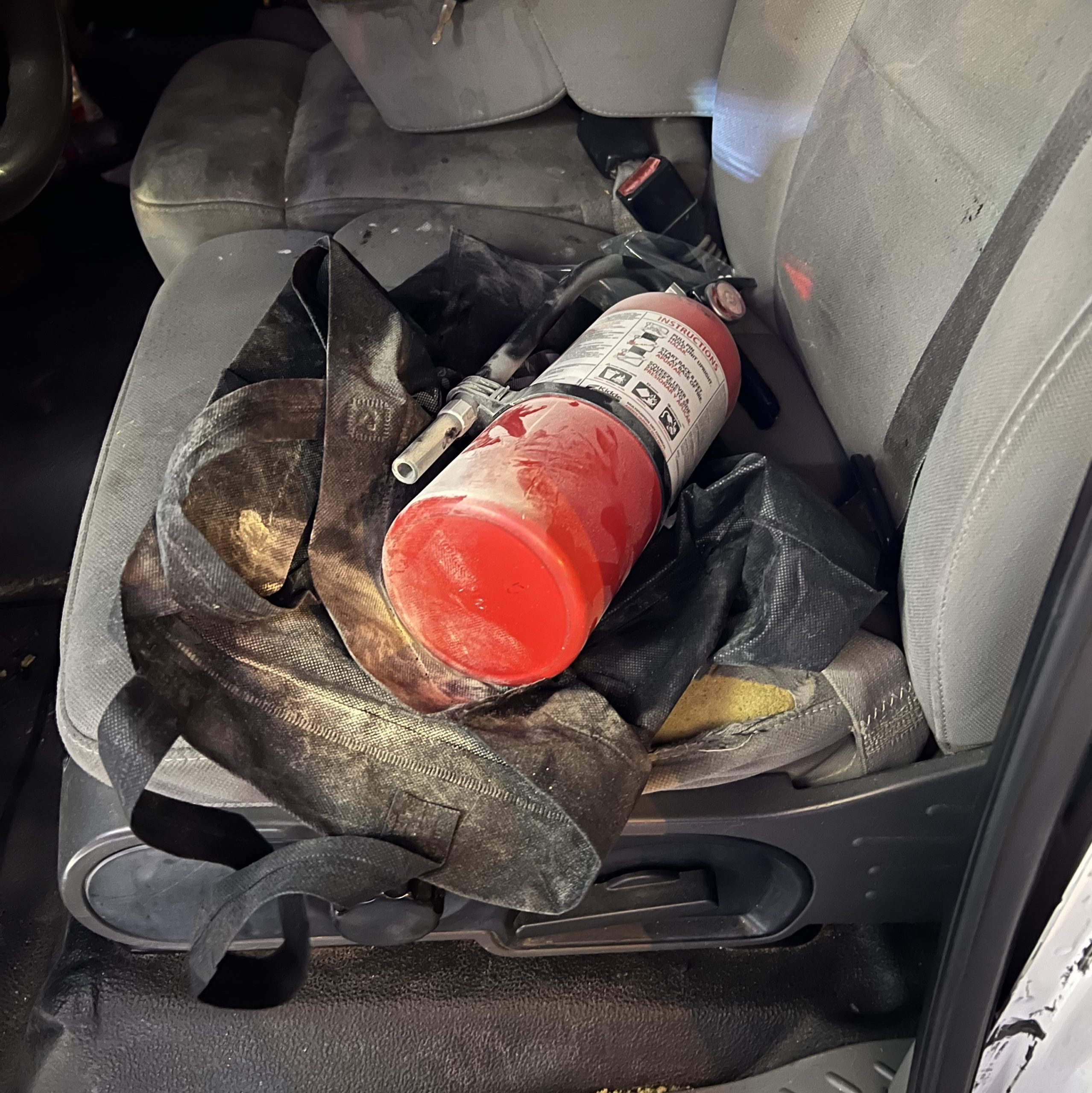 Dusty looking fire extinguisher on a black bag in the back seat of a vehicle