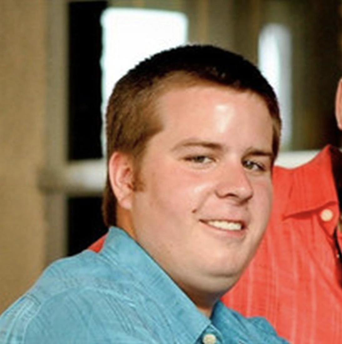 Photo of Taylor Coffman, a young man with auburn buzz-cut hair and a bight blue collared shirt