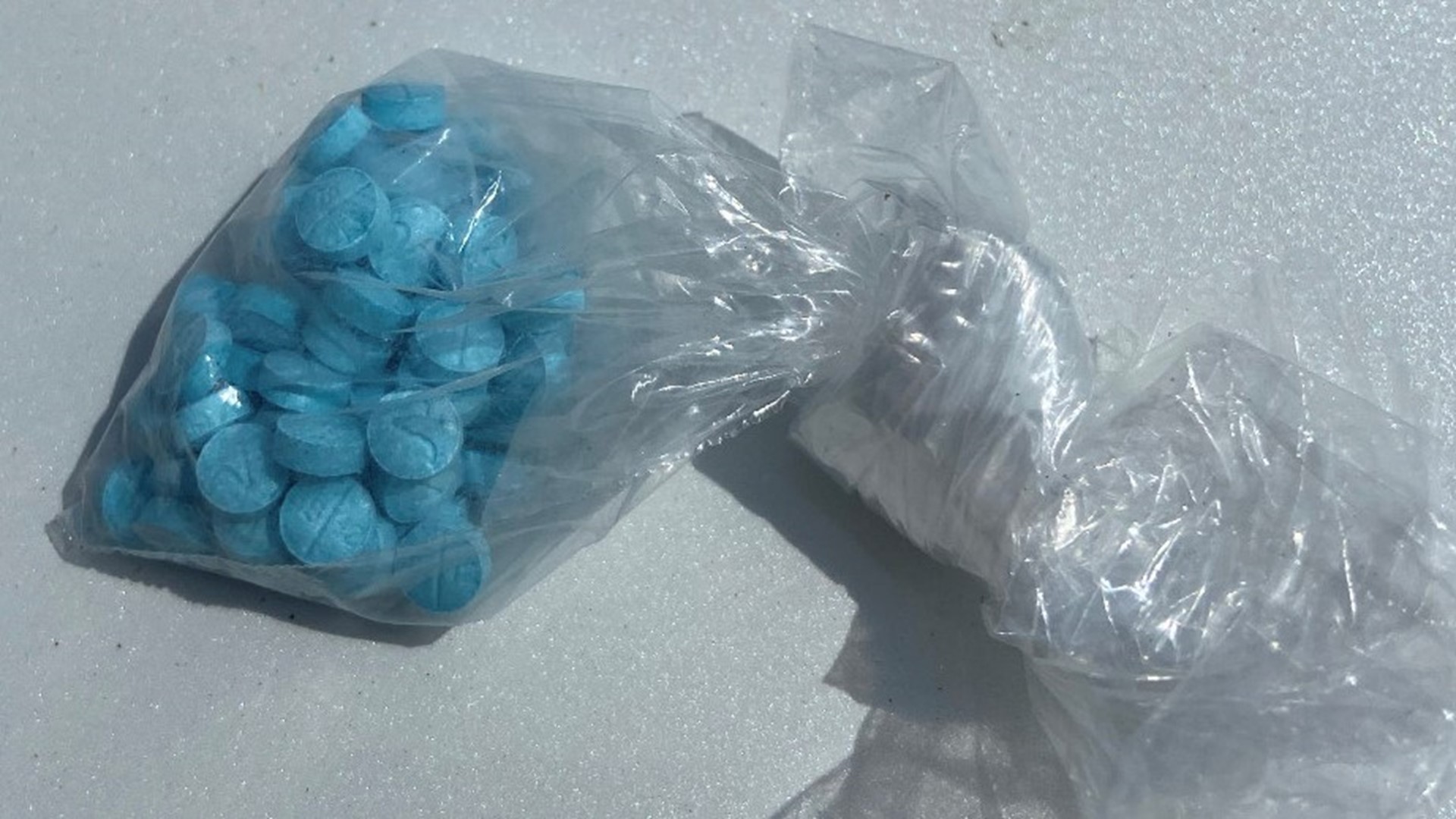 Knotted, clear plastic bag with bright blue pills inside.
