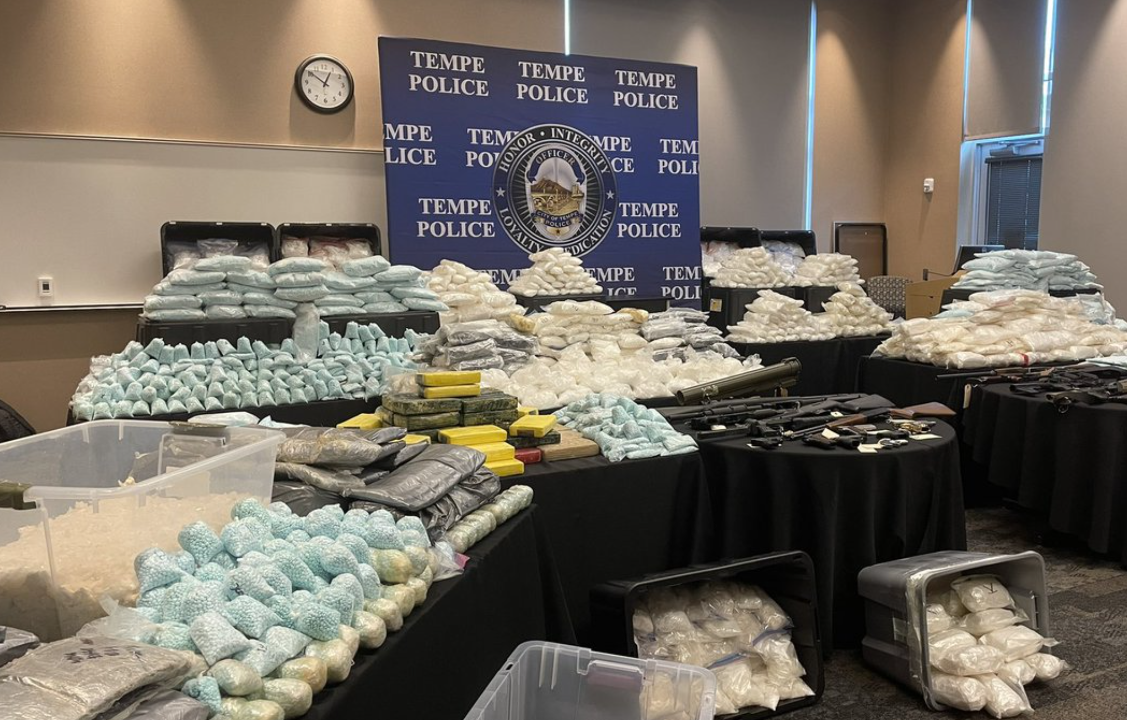 Many, many tables displaying bags of narcotics with a Tempe Police sign behind them