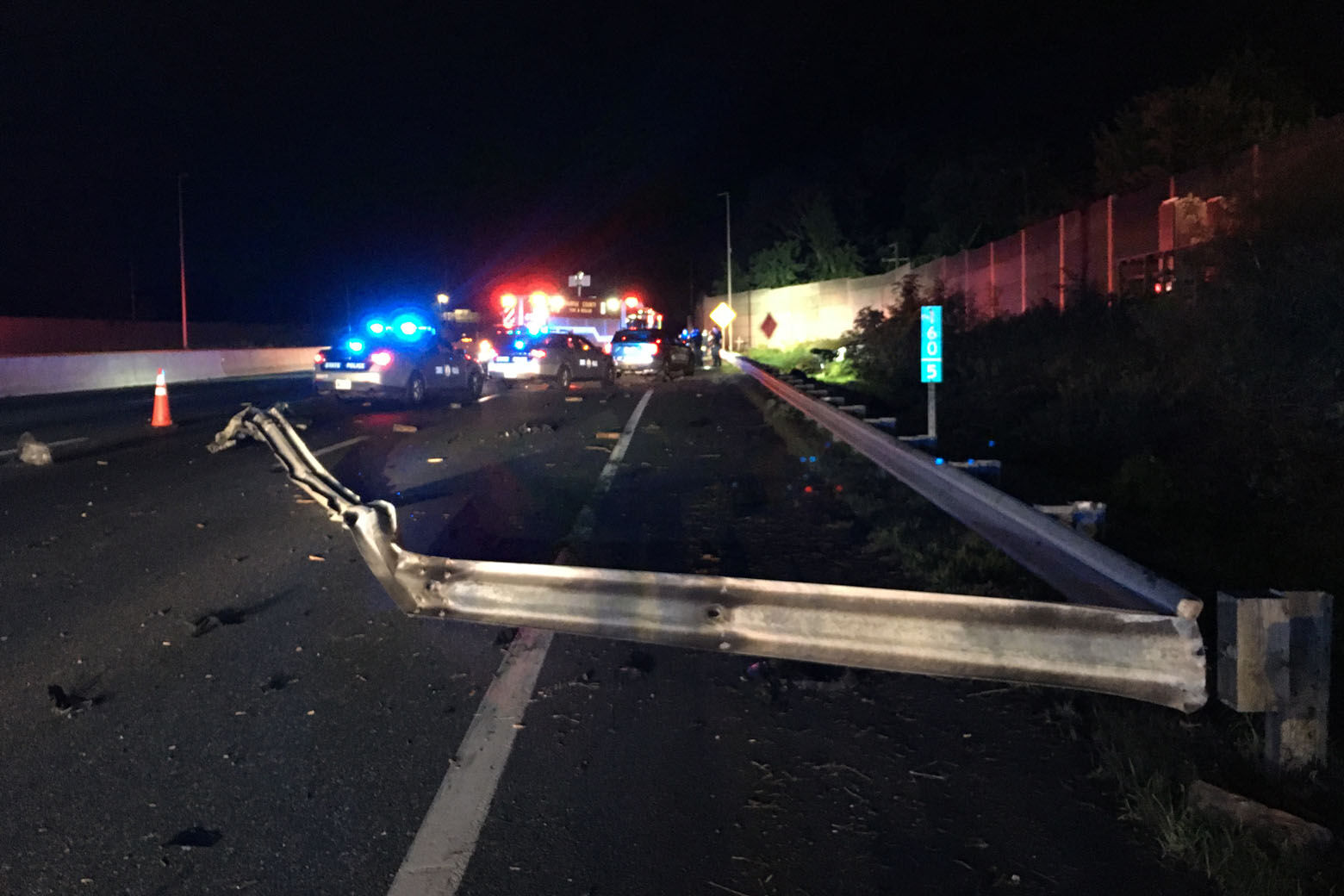 Image of a wrecked car rail and police lights on a dark road