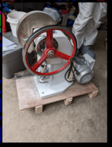 white and red bodied pill press on a wooden base on the floor