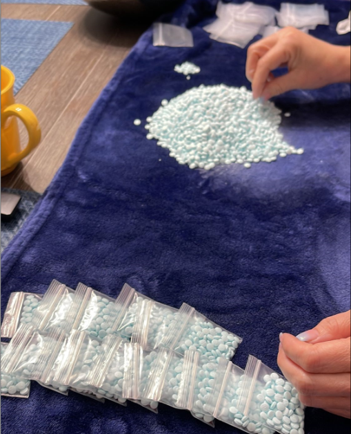 Hands packaging blue pills into baggies.