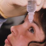 A gloved hand holding container of eye drops above a child's eye