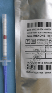 A syringe full of pellets in front of a foil package with a label