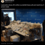 A twitter post showing a police officer standing at the far end of a table with bags of pills and other drug supplies on it. A pill press is visible in the foreground.