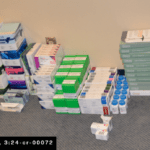 boxes and bottles of medicines stacked on a gray carpet against a wall